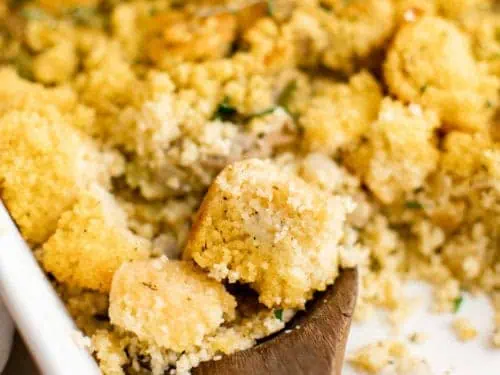 Close up view of a wooden spoon scooping cornbread dressing from a pan.