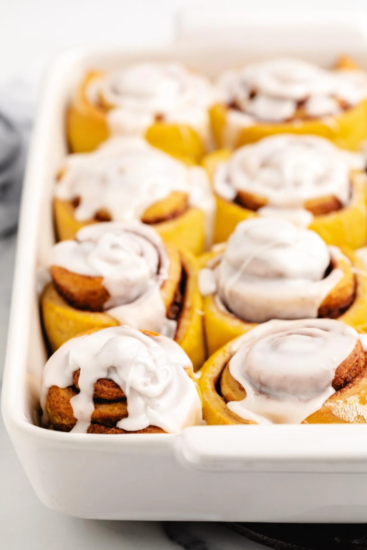 White baking pan filled with iced cinnamon rolls.