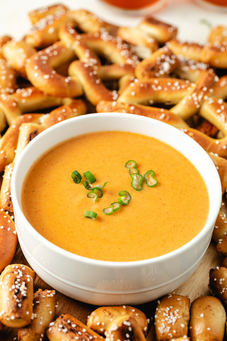 A white bowl of beer cheese dip with soft pretzels.