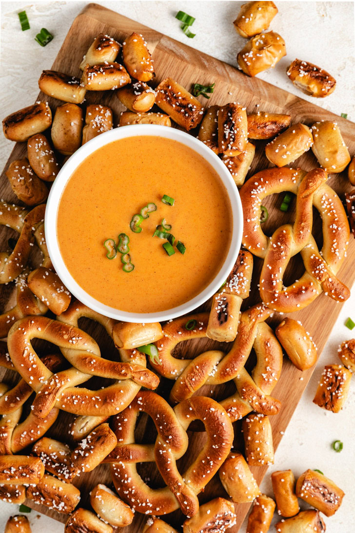 Overhead view of beer cheese dip with pretzels on a wooden board.