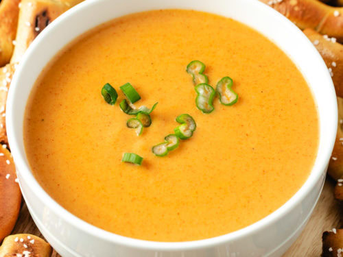 A bowl of creamy beer cheese dip garnished with green onions.