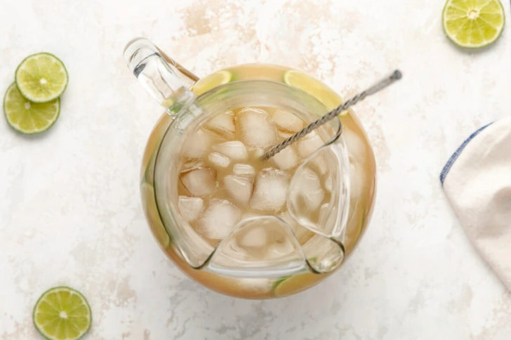 A pitcher of rum with ice and lime slices.
