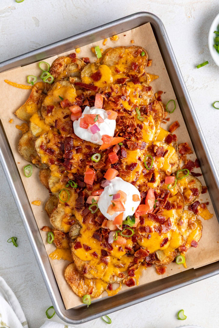 Overhead shot of crispy potatoes with cheese, bacon, sour cream, and green onions.