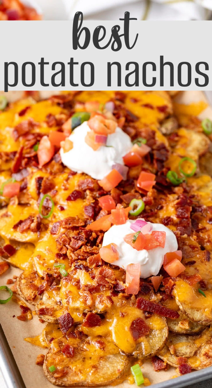 A close-up of fully loaded potato nachos on a parchment-lined baking sheet.