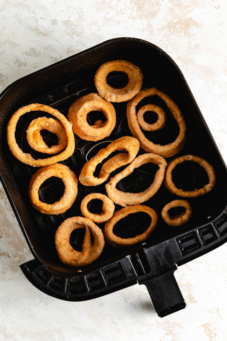 Uncooked onion rings in an air fryer basket.