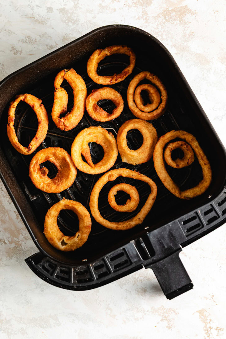 Cooked onion rings in an air fryer basket.