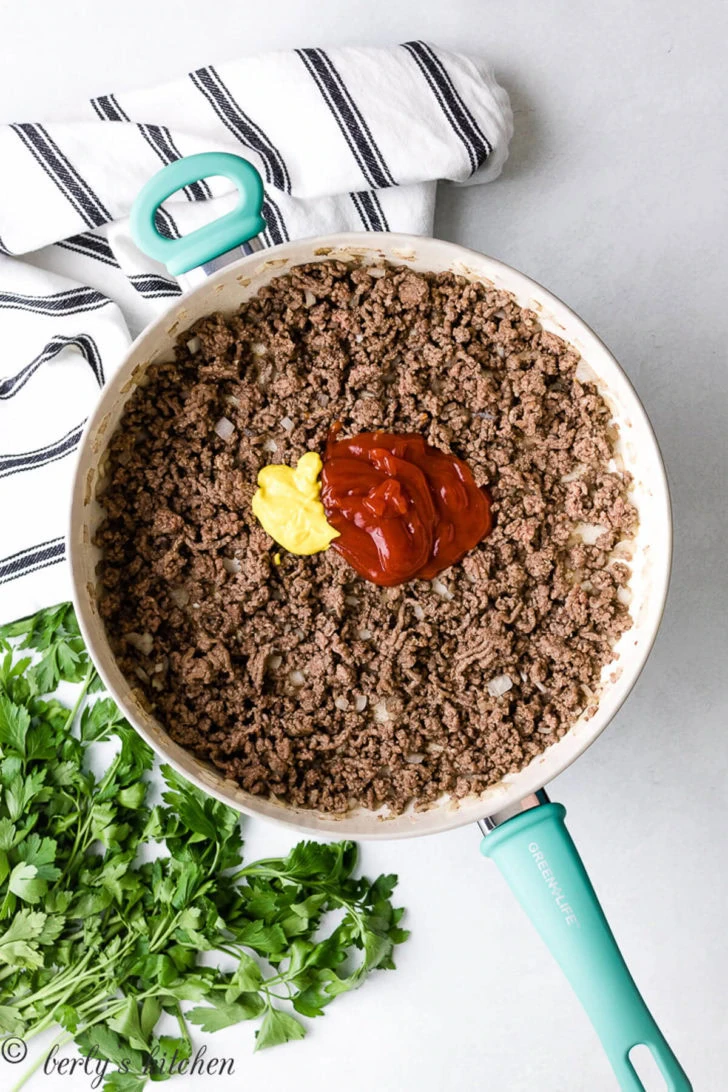 Ketchup and mustard over ground beef in a pan.