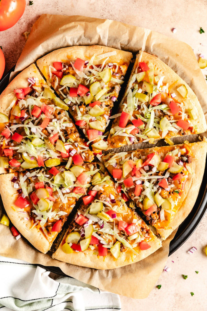 Overhead view of cheeseburger pizza with tomatoes, pickles, and cheese.