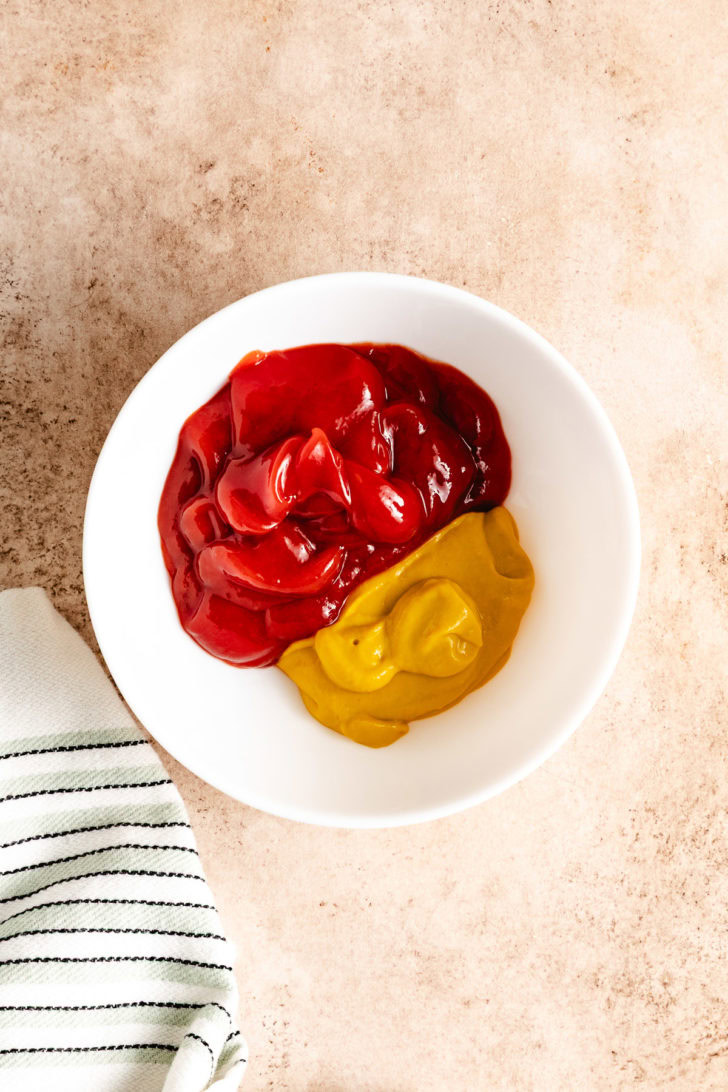 A bowl of ketchup and mustard in a white bowl.