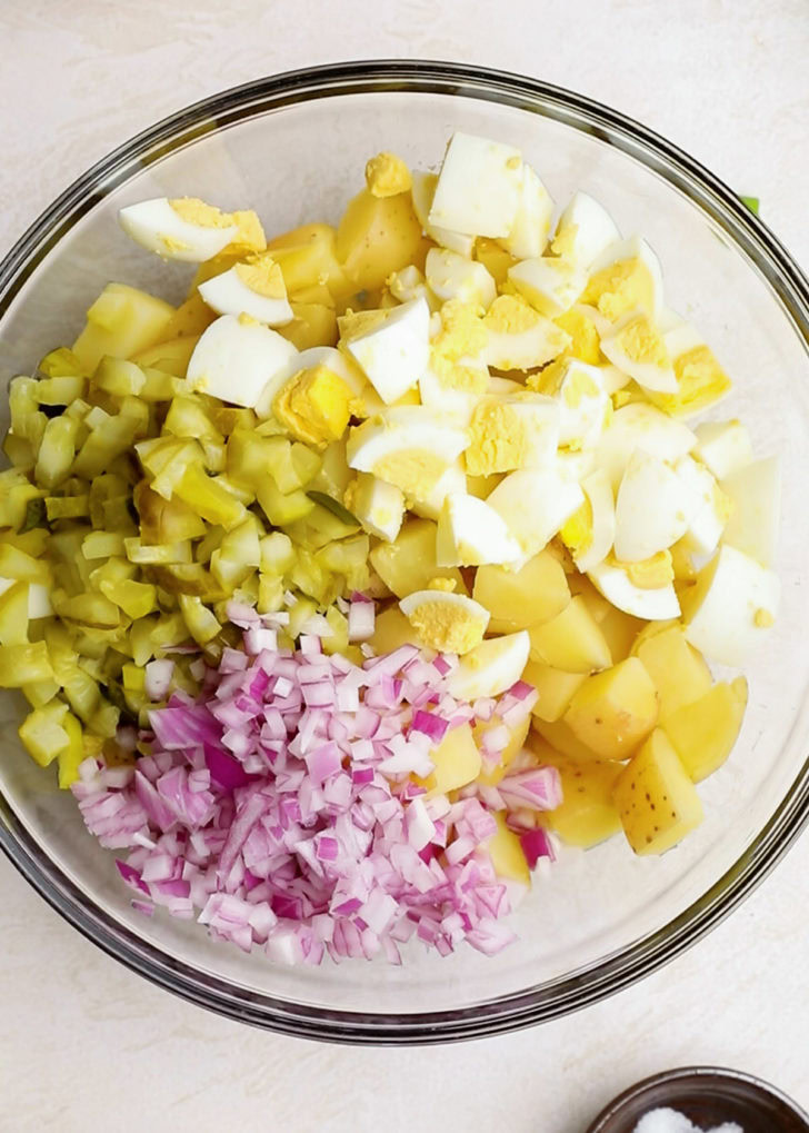 A bowl filled with chopped onions, potatoes, and eggs.