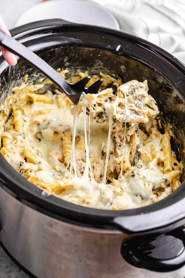 Ladle scooping chicken pasta from a slow cooker.