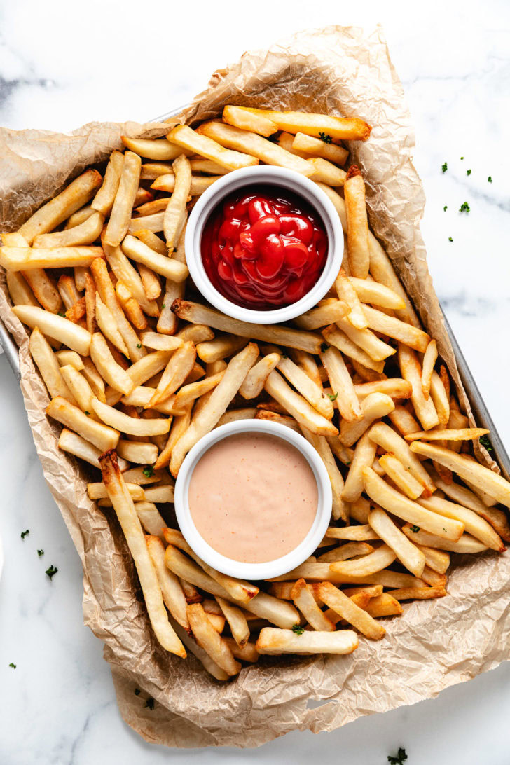 Overhead views of ketchup and dipping sauce next to french fries.