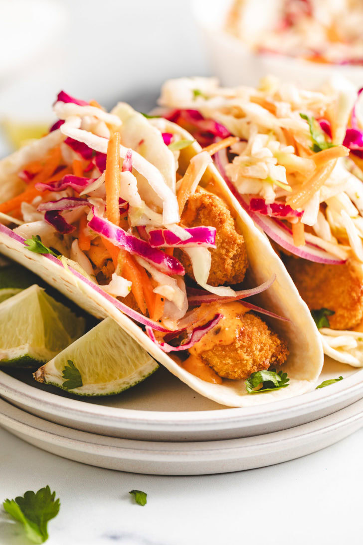 Two fish tacos on a plate with sauce and slaw.