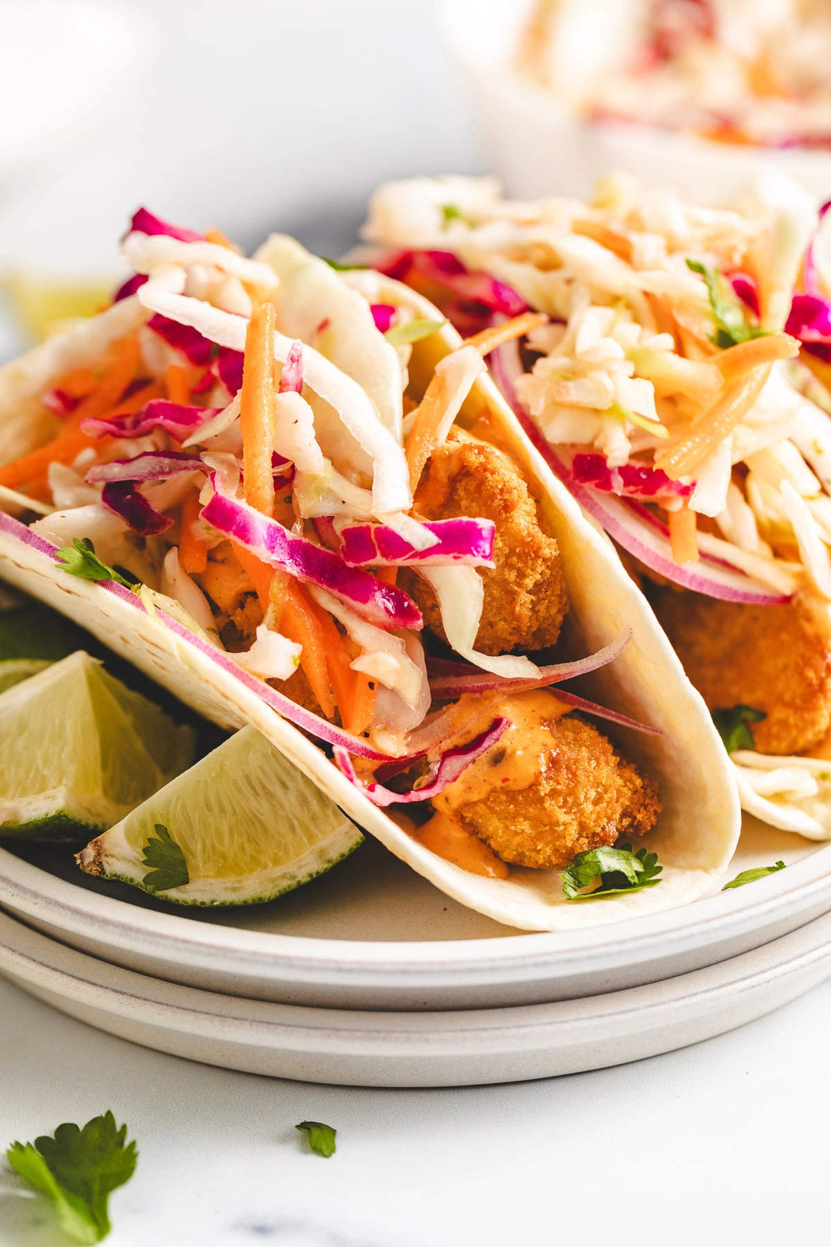 Two fish tacos on a plate with sauce and slaw.