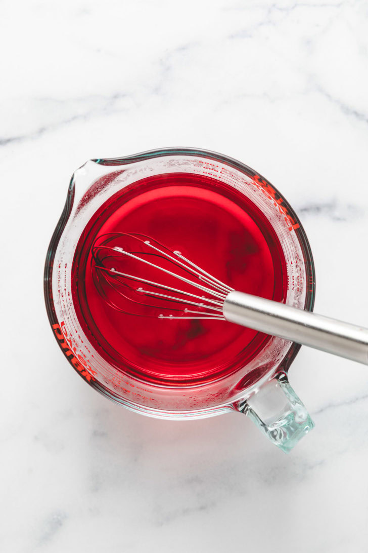 A glass measuring cup with strawberry gelatin.