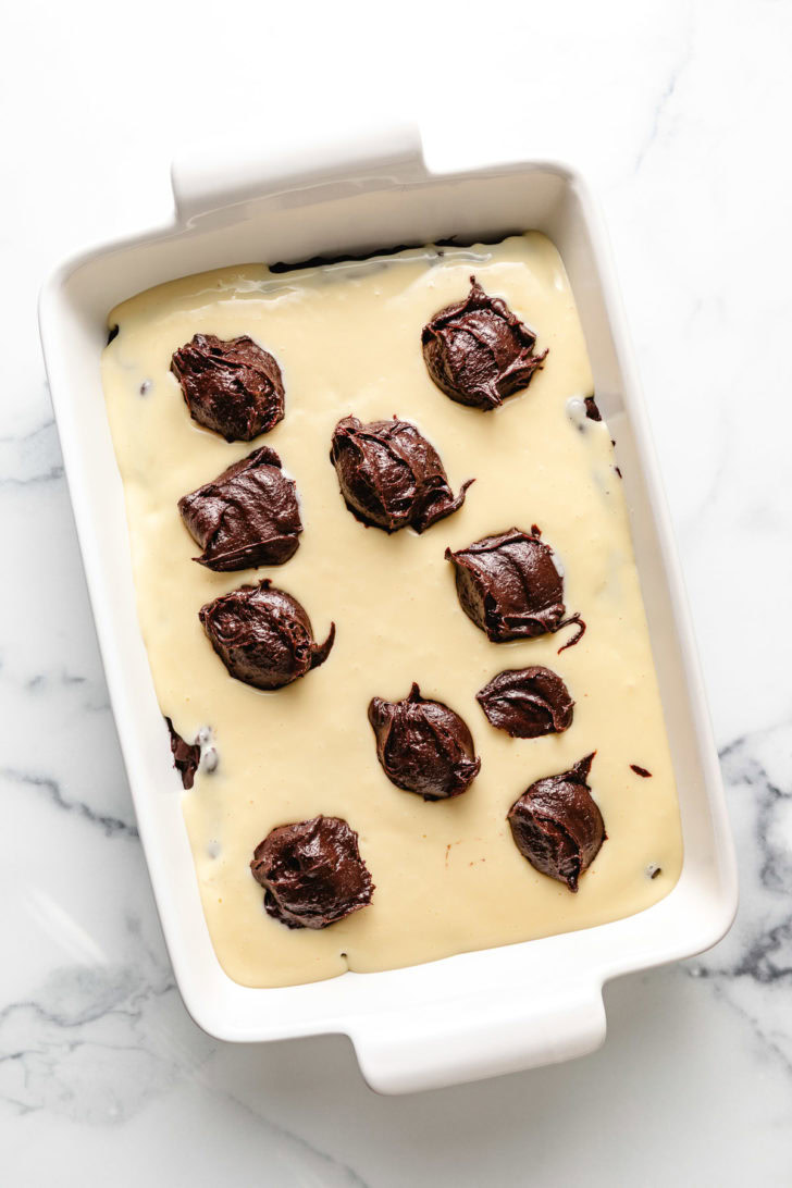 Layered ingredients for cheesecake brownies in a pan.