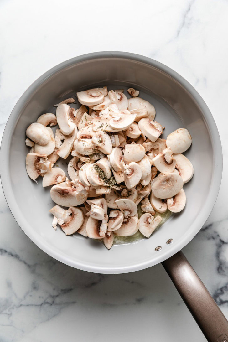 Sliced mushrooms and thyme in a skillet.