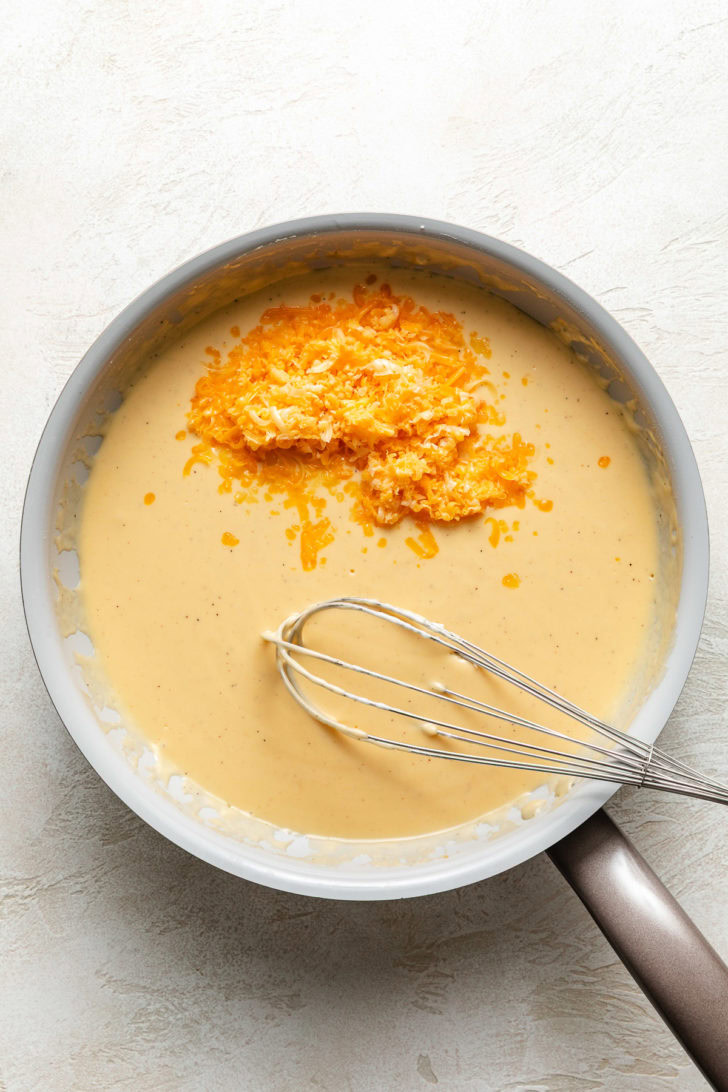 Shredded cheese added to a pan of roux.