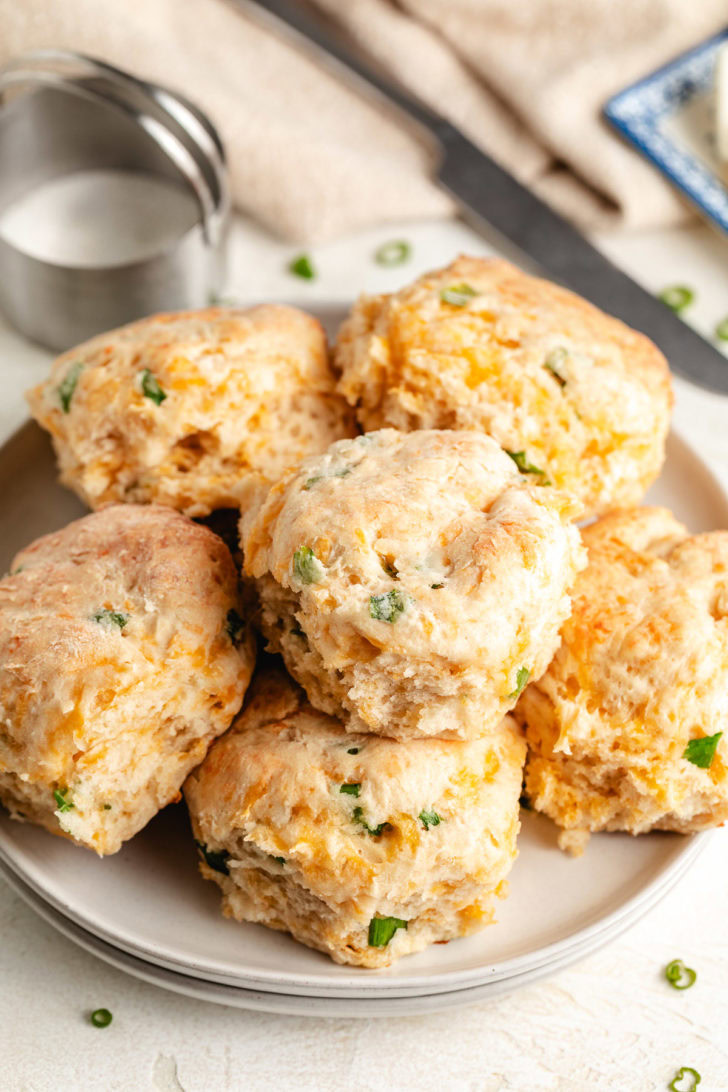 Easy Cheddar Scallion Biscuits Biscuits on a plate next to a biscuit cutter.