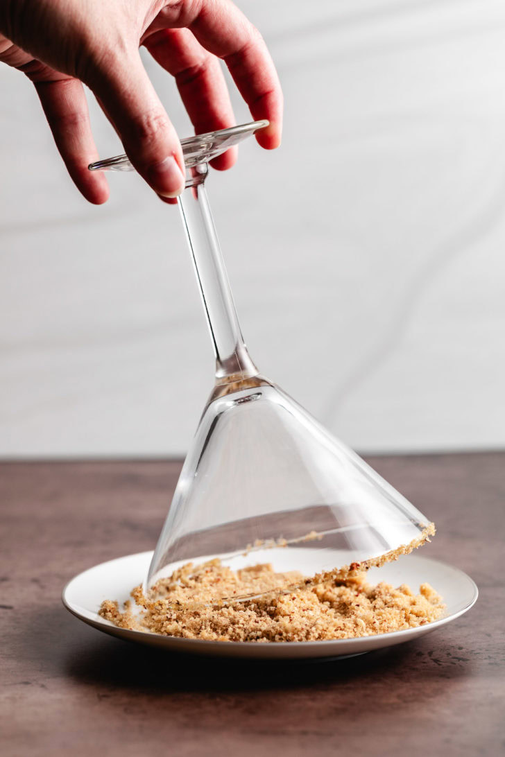 Martini glass being dipped in crushed pecans.
