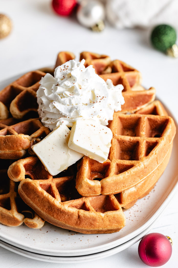 Easiest Eggnog Waffles Eggnog waffles topped with whipped cream and butter.
