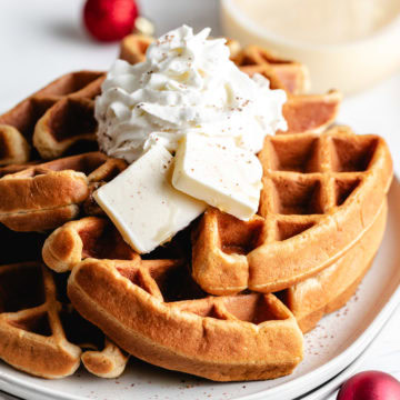 Easiest Eggnog Waffles Eggnog waffles topped with whipped cream and butter.