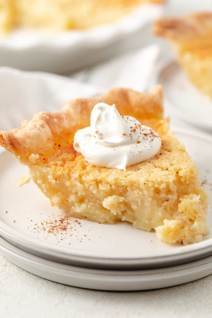 Golden custard pie slice with flaky crust and whipped cream on a white plate.