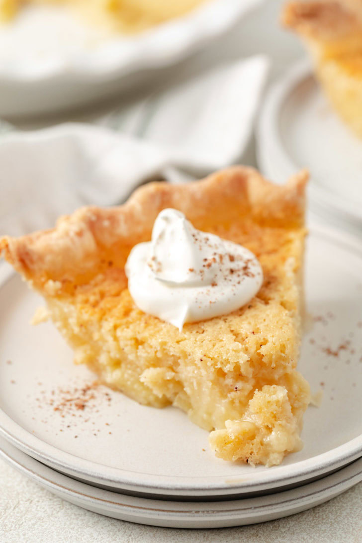 Buttermilk pie slice served on layered plates with whipped cream and a light sprinkle of spice.