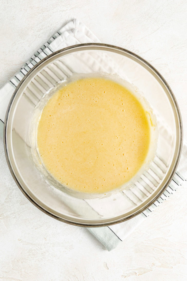 Smooth, pale yellow custard mixture in a glass bowl after the ingredients have been whisked.