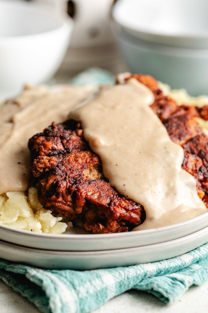 Close-up of crispy cube steak with thick gravy pouring over the top on a dinner plate.