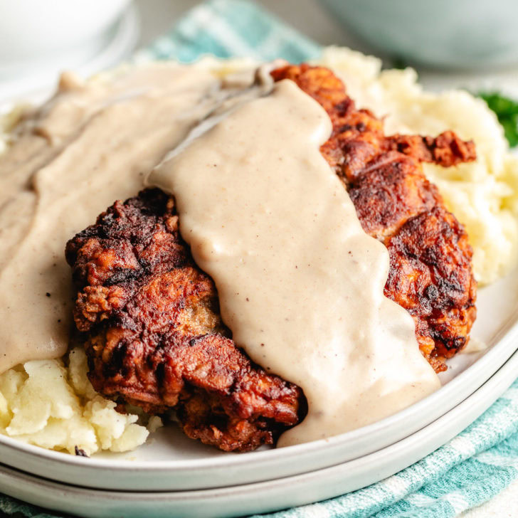 Chicken fried steak with creamy gravy served over mashed potatoes on a plate.