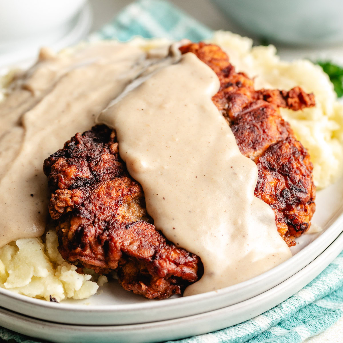 Chicken fried steak with creamy gravy served over mashed potatoes on a plate.