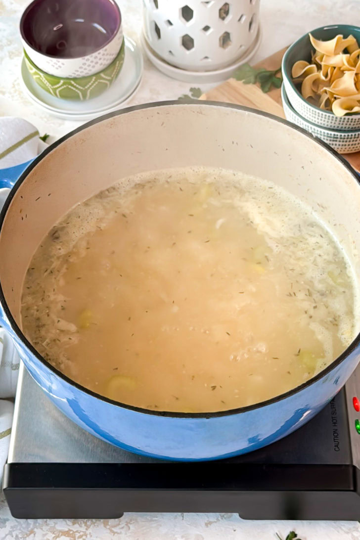 Chicken broth simmering in a blue Dutch oven.