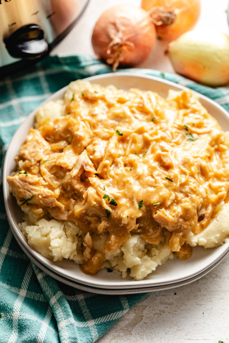 Crockpot chicken and gravy plated over mashed potatoes on a white dish.