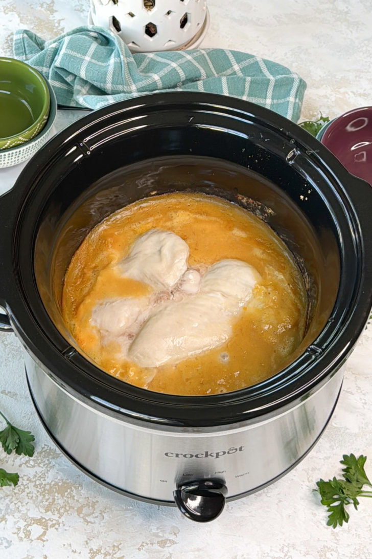 Chicken breasts cooking in a slow cooker surrounded by creamy gravy.