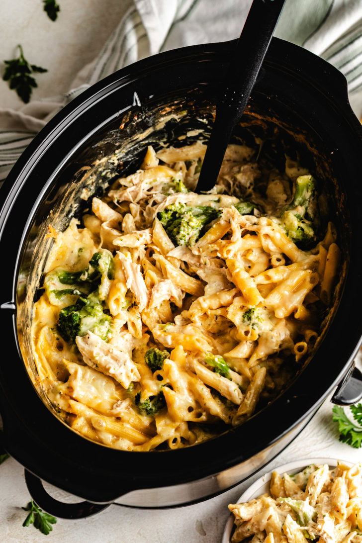 Creamy slow cooker chicken and broccoli pasta in a crock with a spoon.