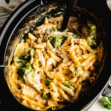 Close-up of crockpot Italian chicken pasta with shredded chicken, broccoli florets, and melted cheese in a slow cooker.