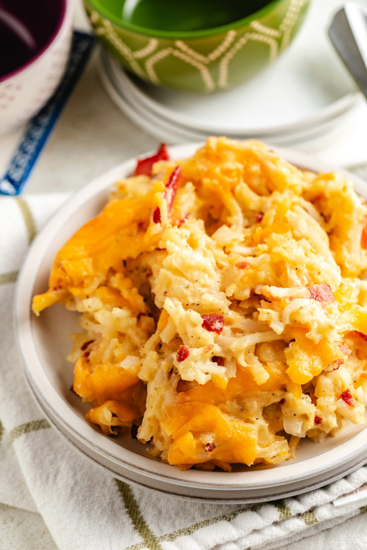 Hashbrown casserole slice on a plate with melted cheese and crispy bacon throughout.