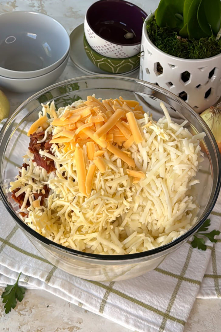 Bowl of shredded potatoes topped with a big layer of shredded cheeses.