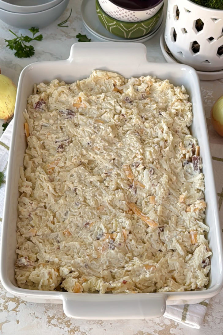 Unbaked hashbrown casserole mixture spread evenly in a white baking dish before going into the oven.