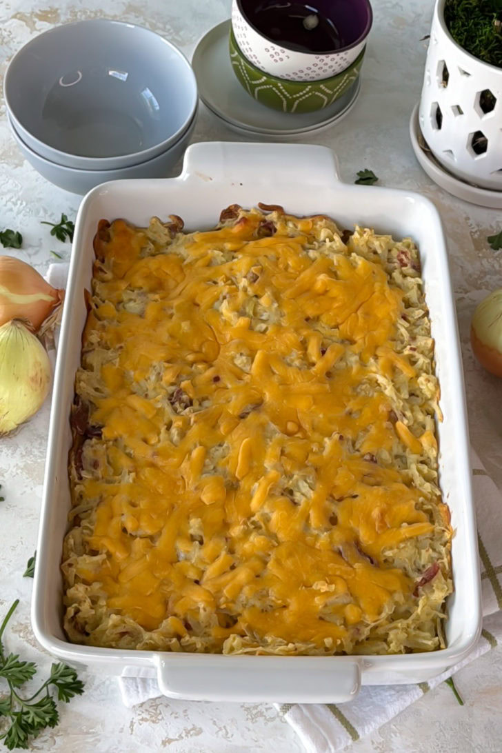 Baked hashbrown casserole in a white casserole dish with melted cheddar on top and golden edges.