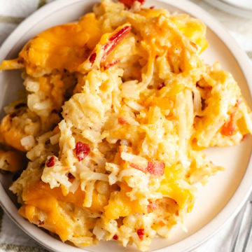 Close-up of a serving of hashbrown casserole on a white plate with melted cheddar and crispy potatoes.