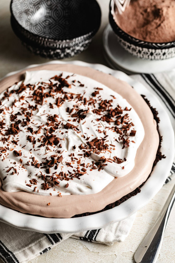 Frozen chocolate cream pie topped with whipped topping and chocolate shavings, styled on a white pie plate.