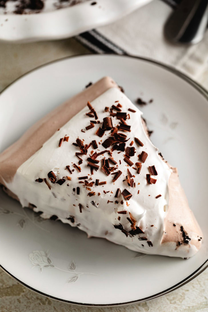 Hot chocolate pie slice on a vintage plate, topped with whipped topping and chocolate curls.