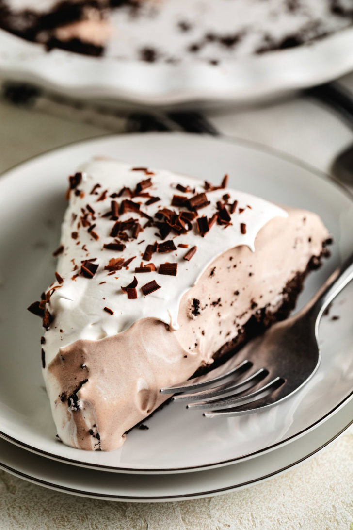 Hot chocolate pie slice on a white plate, showing the chocolate cookie crust and fluffy topping with chocolate curls.