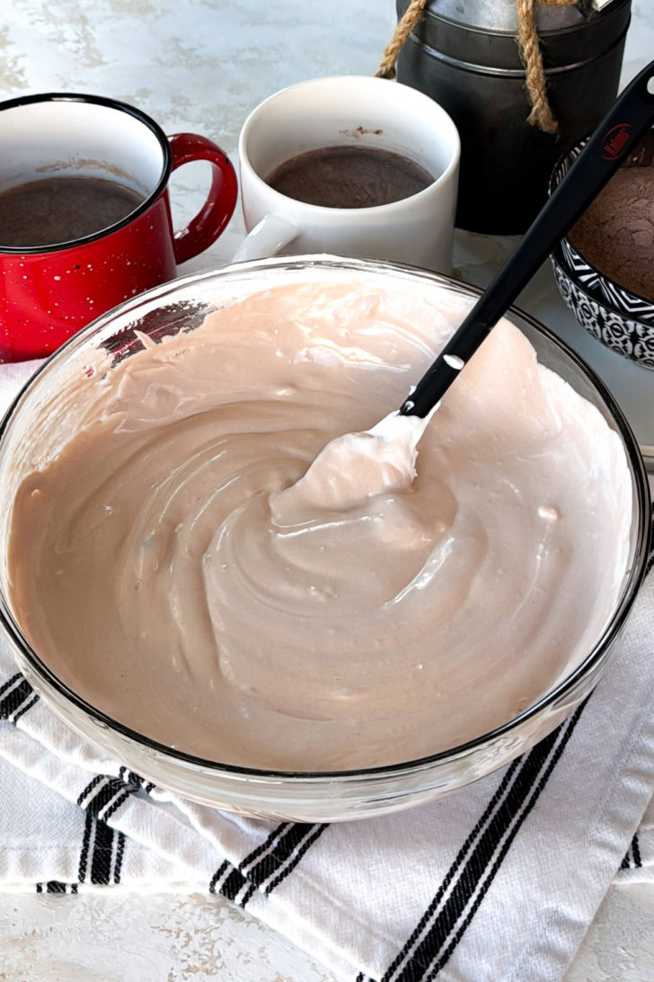 Creamy cocoa mousse-like mixture after folding, shown in a glass bowl with a spatula.