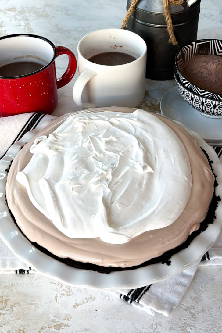 Hot chocolate pie with a whipped topping layer spread over the frozen chocolate filling in a pie dish.