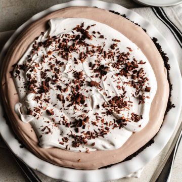 Overhead view of a frozen chocolate cream pie in a white dish, topped with whipped topping and chocolate shavings.