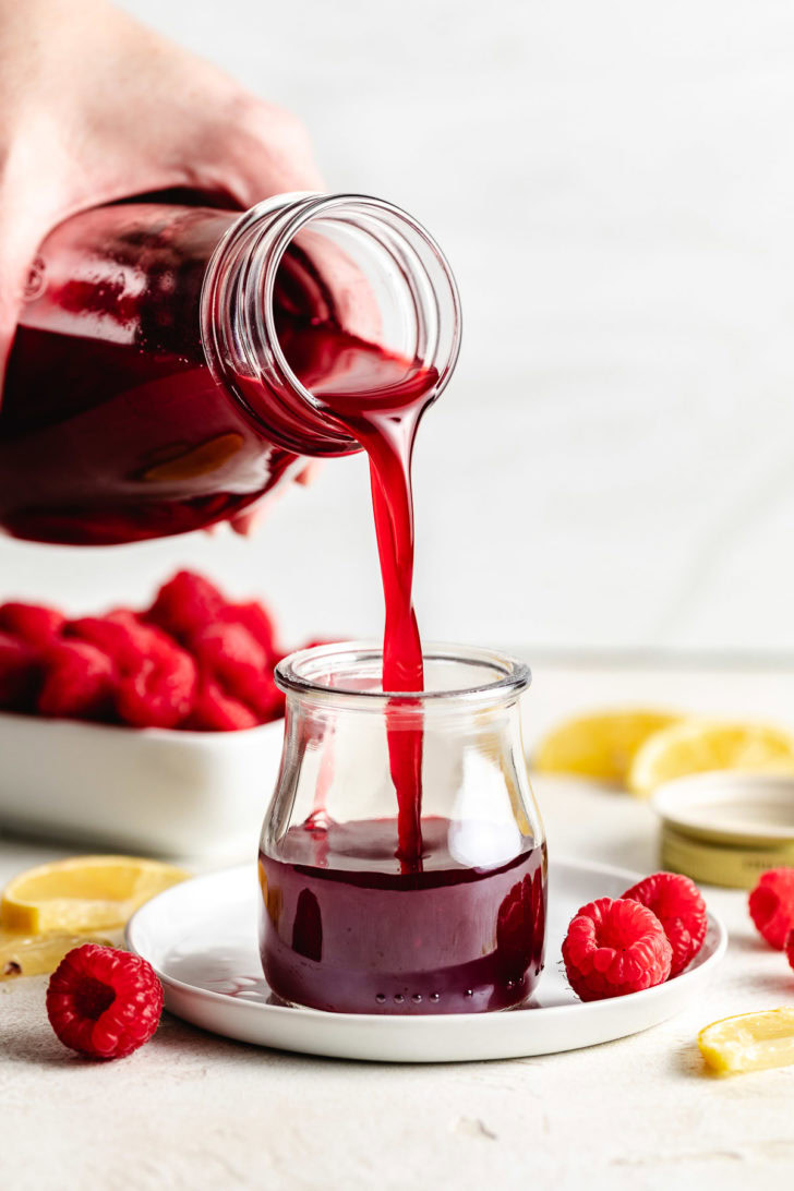 Pouring raspberry simple syrup into glass.