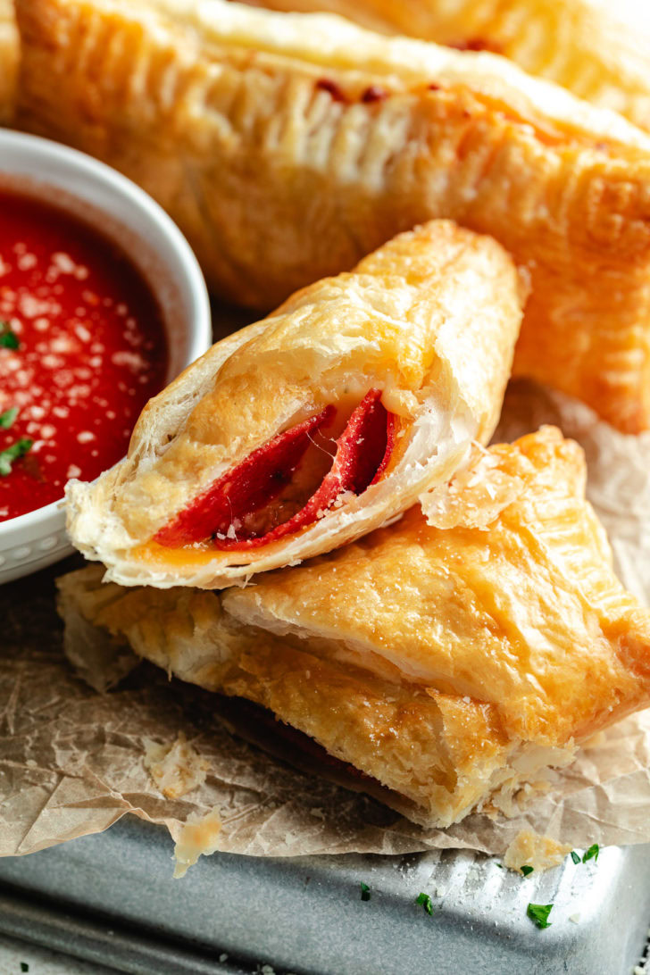 Pepperoni and cheese puff pastry pizza pocket stacked on a tray with marinara dipping sauce.